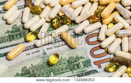 White and yellow macro drug pills and fish oil capsules on one hundred dollars banknotes as a background. Money and medicine still life concept.