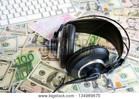Professional music headphones with white keyboard on dollars and euro as a background. Money and technology still life concept.