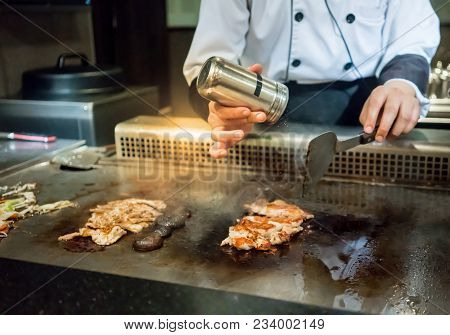 Hand Of Chef Adding Salt Into The Steak On Hot Pan In Front Of Customers. Japanese Tepanyaki Steak
