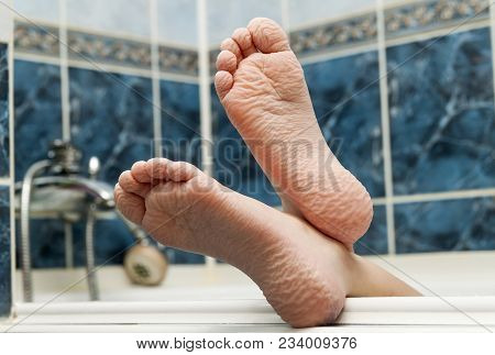 Wrinkled Bare Feet Coming Out From A Bathtub. Young Person Getting A Bath Feet Close-up Indoor In Ba