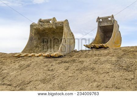 Low Angle Shot Showing Two Old Dredger Buckets On Loamy Ground In Front Of Partly Blue Sky