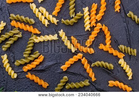 Raw Colored Spiral Pasta On Slate. Uncooked Three-colored Fusilli Durum Wheat Pasta On Black Texture