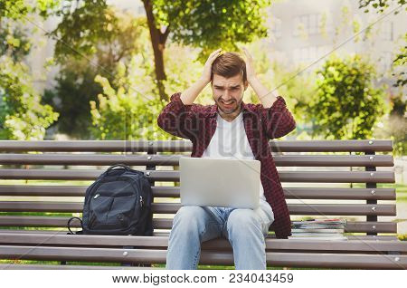 Desparate Handsome Young Man Using Laptop Outdoors. Unhappy Student Raising His Hands To His Head. T