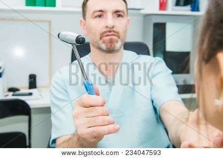 Male Neurologist Doctor Inspecting Young Female Patient's Nervous System Using A Hammer. Neurologica