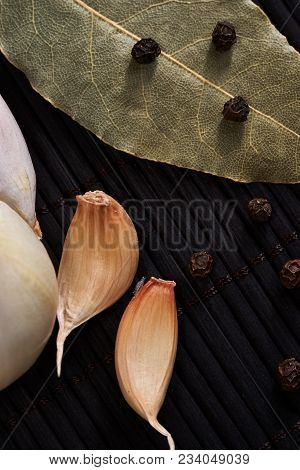 Onion, Garlic, Black Pepper And Bay Leaf On A Black Table