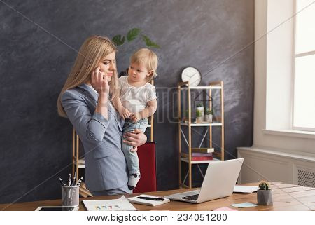 Happy Mother Working At Office With Her Baby. Young Woman Talking On Phone And Using Laptop While Sp