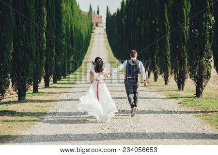 Happy Stylish Smiling Couple Walking In Tuscany, Italy On Their Wedding Day.