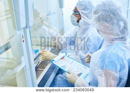 Modern Qualified Team Of Biologists Holding Experiment With Plant In Laboratory Equipped With Isolat