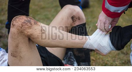 Soccer, football concept. Injured footballer lay down on field. Physiotherapist puts bandage on his ankle. Blurred background, close up view.