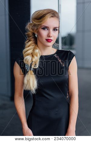 Attractive Lady With Blong Hair In Long Evening Dress Stands Next To The Building With Mirror Window