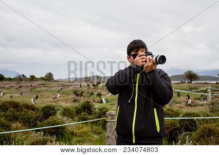 Photographer Standing With Camera In Hand In Martillo Island, With Many Penguins In The Background, 