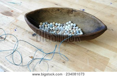 Weaving Of Beads. Blue Beads In A Wooden Bowl Shaped Like A Boat On A Wooden Table