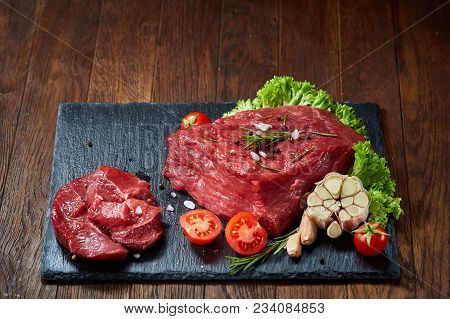 Yummy Composition Of Raw Beefsteak On Slate Board With Rosemary, Spicies, Garlic, Tomatoes, Letucce 