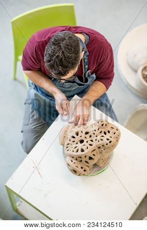 Topview of Ceramist Dressed in an Apron Sculpting Statue from Raw Clay in the Bright Ceramic Workshop.