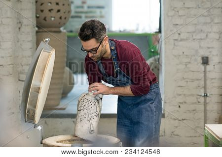 Ceramist Dressed in an Apron Placing Clay Sculpture in the Electric Oven.