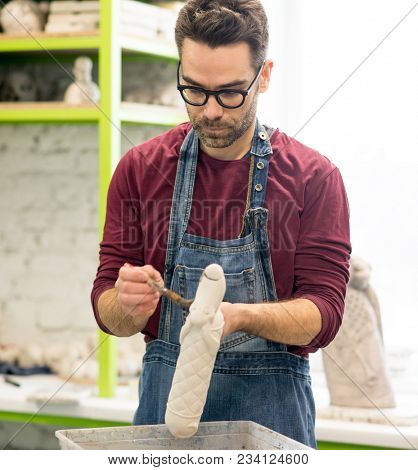 Portrait of Ceramist Dressed in an Apron Working on Clay Sculpture in the Bright Ceramic Workshop.