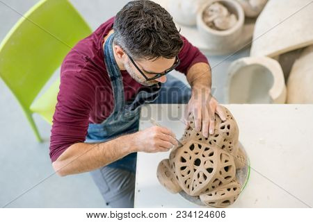 Topview of Ceramist Dressed in an Apron Sculpting Statue from Raw Clay in the Bright Ceramic Workshop.