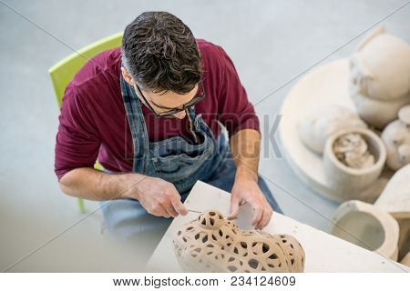 Topview of Ceramist Dressed in an Apron Sculpting Statue from Raw Clay in the Bright Ceramic Workshop.