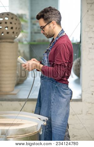 Ceramist Dressed in an Apron Setting the Electric Oven for Drying the Clay Sculpture Using the Control Console.