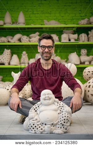 Portrait of Smiling Young Ceramist in the Bright Modern Ceramic Workshop Sitting Next to his Sculpture. Small Business Concept.