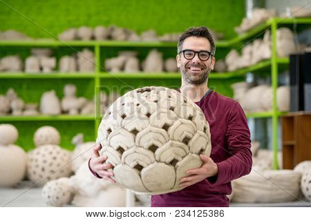 Portrait of Young SmilingCeramist in the Bright Modern Ceramic Workshop Holding his Sculpture. Small Business Concept.