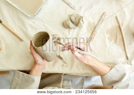 Working master processing handmade clay mug with special handtool over table