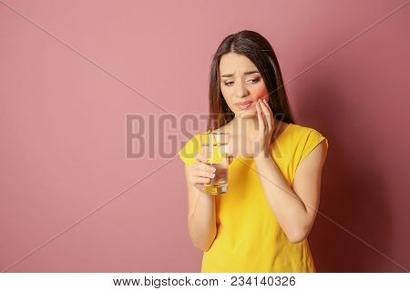 Woman With Sensitive Teeth Holding Glass Of Water On Color Background