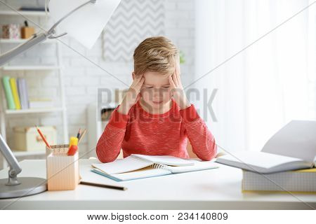 Little Boy Suffering From Headache While Doing Homework At Table Indoors