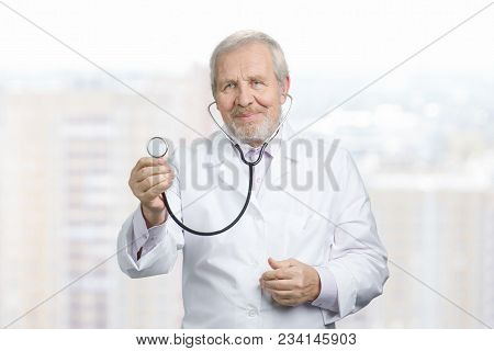 Old Doctor Surgeon Showing Stethoscope. Listeting Your Hearbeat Or Lungs. Blurred City Background.