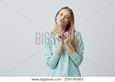 Happy Lovely Female With Blonde Long Hair Showing Love Signs With Her Hands Cupped In Heart Shape. C