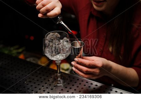 Barmaid Is Standing At The Bar And Pouring Red Wine Into A Glass, Preparing An Alcoholic Cocktail