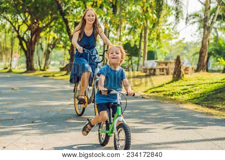 Happy Family Is Riding Bikes Outdoors And Smiling. Mom On A Bike And Son On A Balancebike.