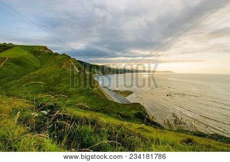 A View To Scenic Coastine Of Zumaia, Spain From A Summer Meadow With Summer Plants And Flowers.