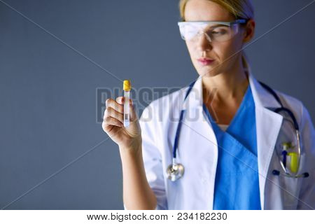 Female medical or research scientist or doctor using looking at a test tube of clear solution in a lab or laboratory.
