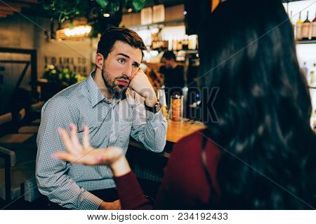 Girl Sitting In Front Of Young Guy And Talking To Him. He Looks Bored. Man Is Not Interested In Conv