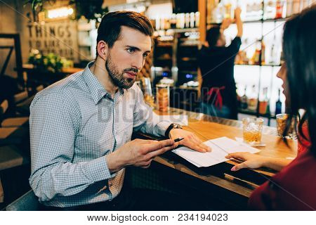 A Business Meeting Of Two People In A Bar. Man Is Explaining Something To Woman. She Is Listening To