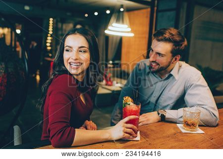 Apicture Of Happy Girl Sitting With A Handsome Guy In The Bar. She Is Looking Somewhere Aside And Sm