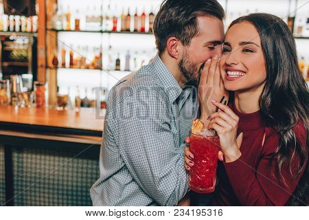 Beautiful People Are Sitting Very Close To Each Other In Bar. He Is Whispering Something In Her Ear 