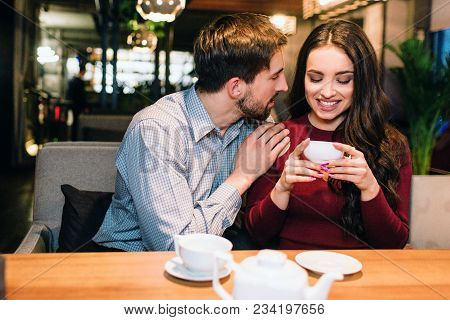 Attractive Girl Is Sitting On The Sofa In Restaurant And Drinking Some Tea While Her Partner Has Put