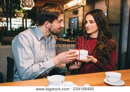 Picture Of Man Giving A Present To A Woman. They Are Looking To Each Other And Smiling A Bit. They A