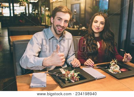 Advertising Picture Of Man And Woman Sitting At The Table With Some Food On It. They Are Looking To 
