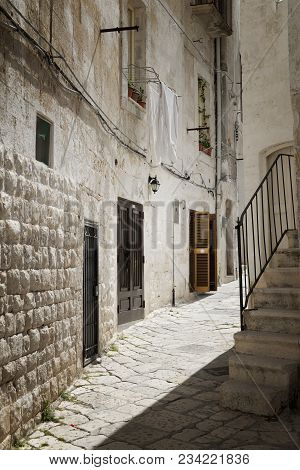 Laundry Day In Italy With White Blankets Hanging To Dry From A Stone House In A Cobblestone Alley In