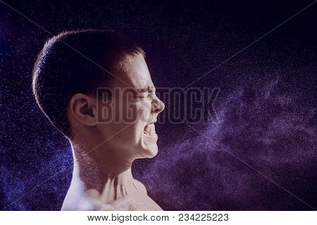 Pre Teen Boy Angrily Screams Into A Spray Of Water Against A Black Background. Toned Image.