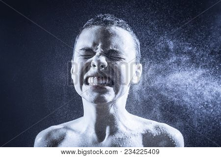Pre Teen Boy Angrily Screams Into A Spray Of Water Against A Black Background. Toned Image.