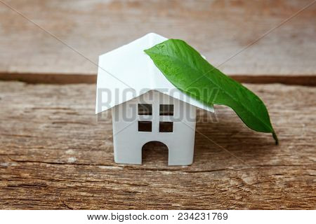 Miniature White Toy Model House With Green Leaves On Wooden Backgdrop. Eco Village, Abstract Environ