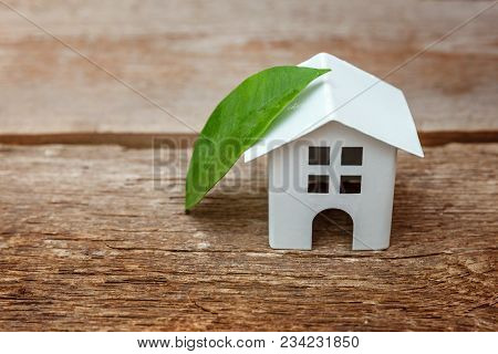 Miniature White Toy Model House With Green Leaves On Wooden Backgdrop. Eco Village, Abstract Environ