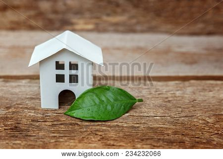 Miniature White Toy Model House With Green Leaves On Wooden Backgdrop. Eco Village, Abstract Environ
