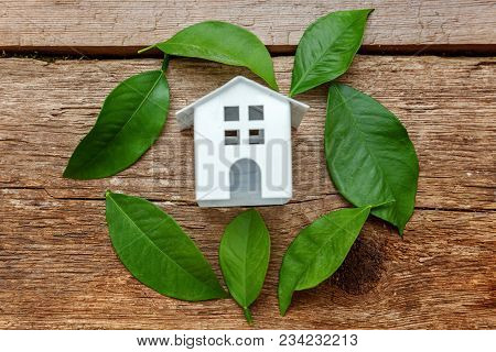 Miniature White Toy Model House With Green Leaves On Wooden Backgdrop. Eco Village, Abstract Environ