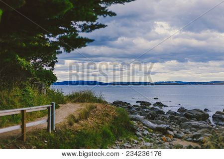 Deserted Beach In Hobart, Tasmania With Rocks And Walkpath In The Foreground On An Overcast Day With