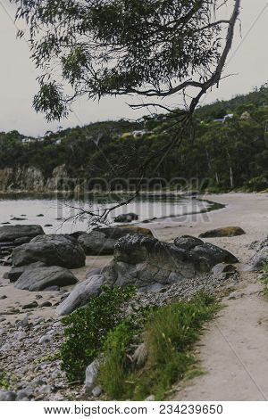 Deserted Beach In Hobart, Tasmania With Rocks And Walkpath In The Foreground On An Overcast Day With